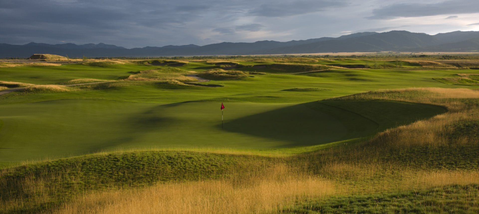 A golf course with green grass and mountains in the background.