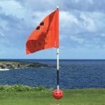 A red flag on the beach with a ball in front of it.