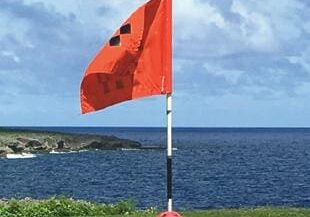 A red flag on the beach with a ball in front of it.